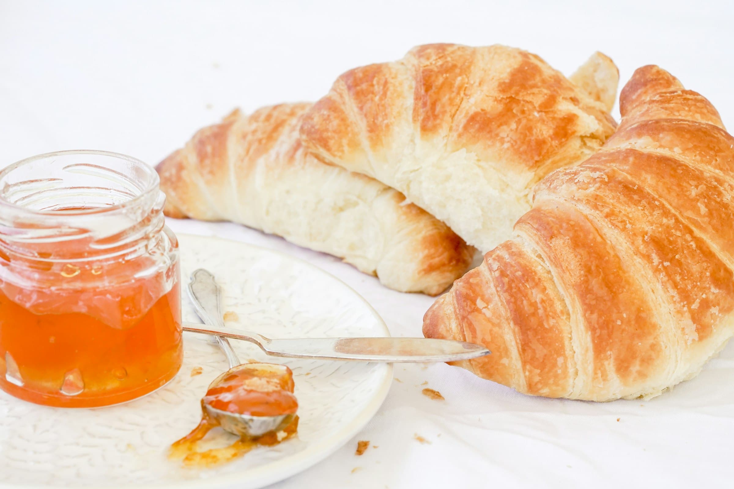 A croissant on a plate beside a jar of jam